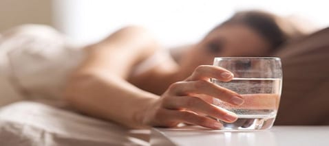 Woman reaching for glass of water to fight night sweats